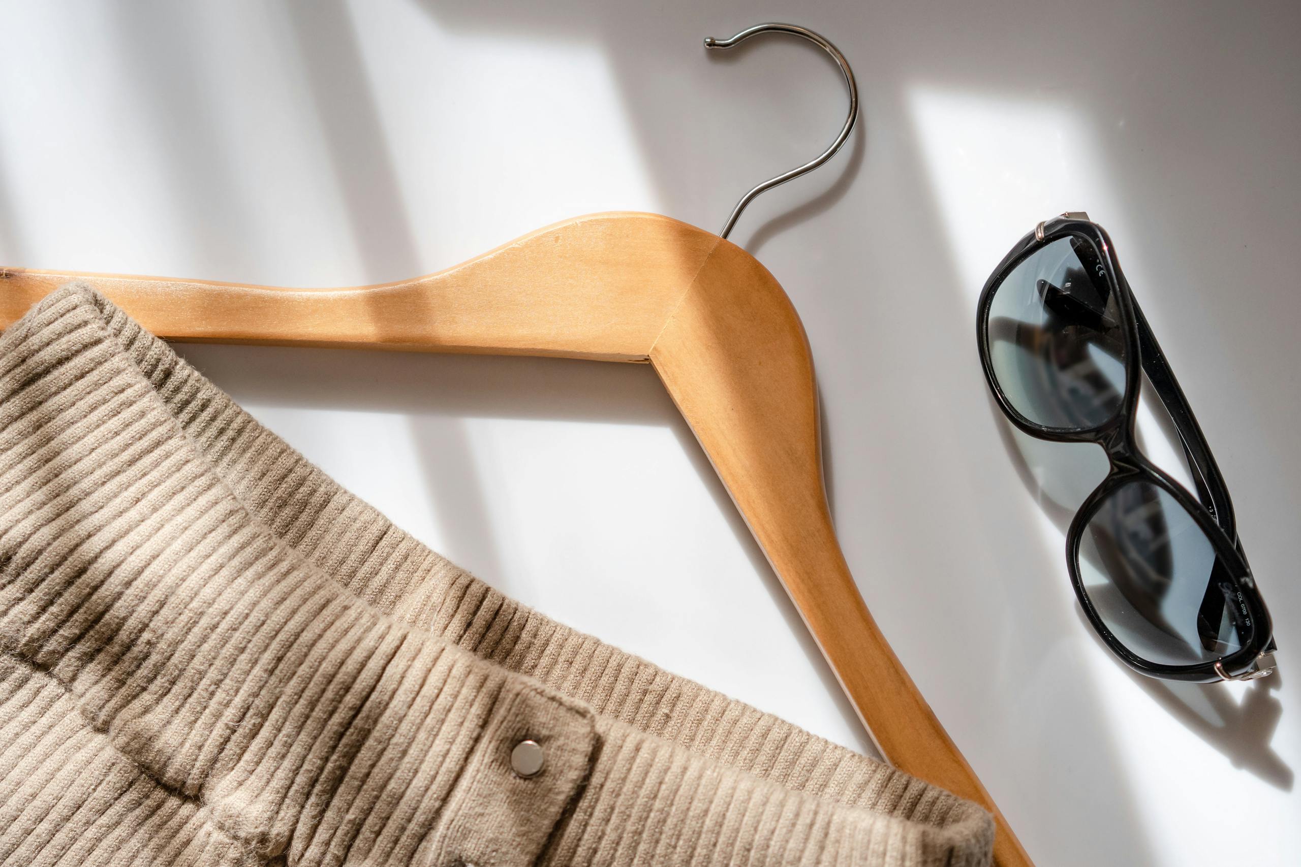 Flat lay of a corduroy skirt, sunglasses, and a wooden hanger on a white surface.